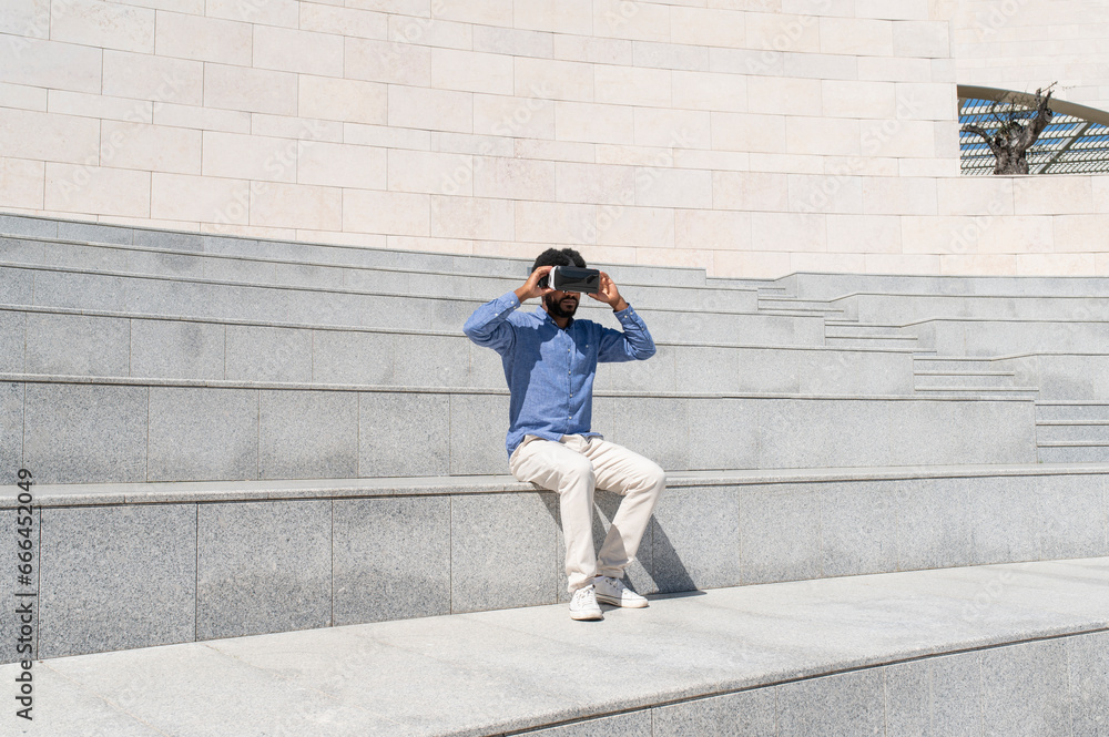Young man sitting on steps wearing virtual reality simulator Young man sitting on steps wearing virtual reality simulator