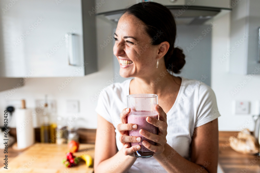 Cheerful woman holding glass of milkshake at home Cheerful woman holding glass of milkshake at home