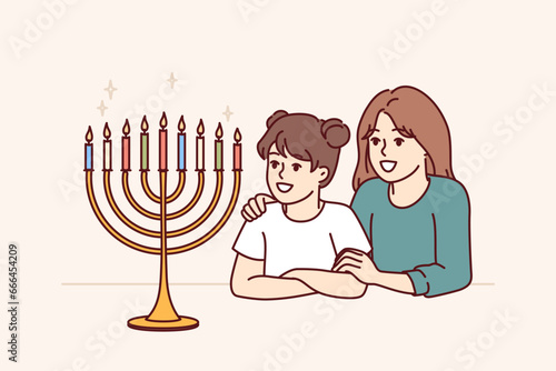 Preteen girls sisters look at menorah with burning candles and rejoice at approach of holiday of hanukkah. Menorah on table near two happy children symbolizes jewish religion and honoring traditions photo