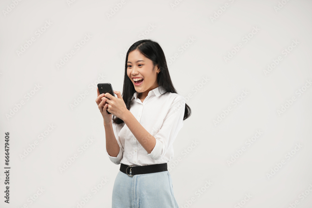 The photo of Surprised young Asian lady using mobile phone with positive expression, smiles broadly, dressed in casual clothing. Isolated on a white background. The photo of Surprised young Asian lady using mobile phone with positive expression, smiles broadly, dressed in casual clothing. Isolated on a white background.