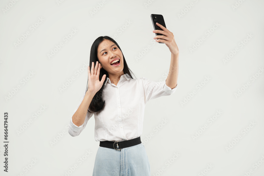 Smiling adorable young Asian female taking a selfie photo on her smartphone with a positive expression looking at the camera. Smiling adorable young Asian female taking a selfie photo on her smartphone with a positive expression looking at the camera.