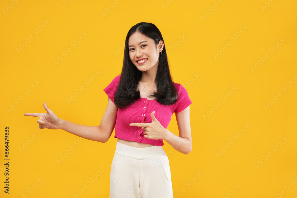 Photo of excited Asian woman pointing aside at copy space, wearing a pink t-shirt and isolated on a yellow background. Photo of excited Asian woman pointing aside at copy space, wearing a pink t-shirt and isolated on a yellow background.