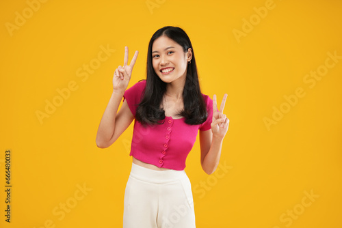 Photo of a young Asian woman carefree showing peace or enjoying life, smiling broadly, isolated on a yellow background.