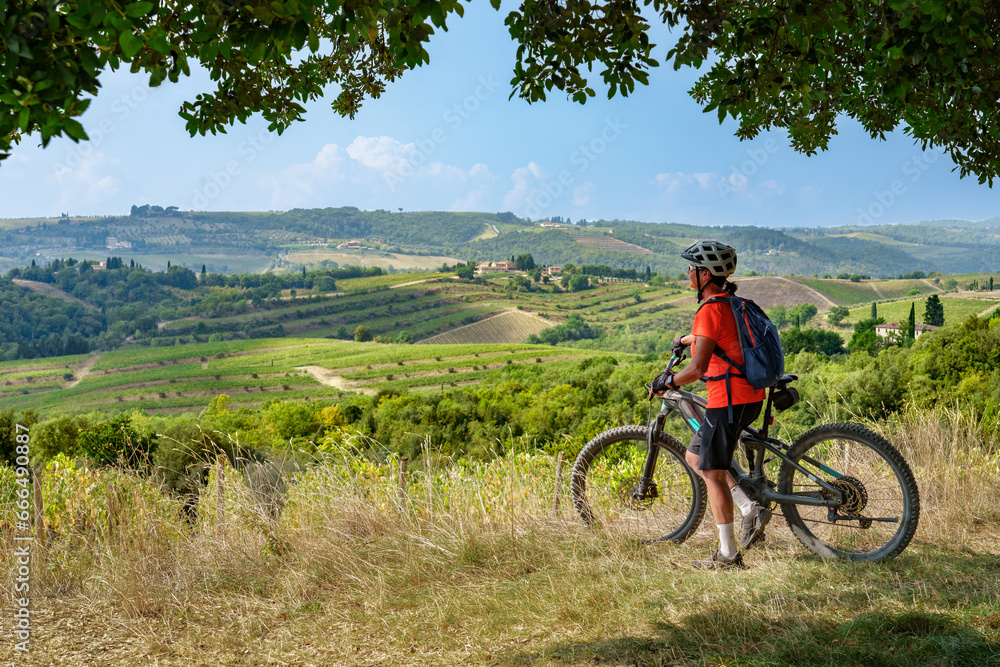 Fototapeta premium nice senior woman riding her electric mountain bike below a huge stone oak tree in the Ghianti Area of Tuscany, Italy