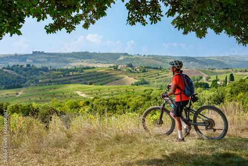nice senior woman riding her electric mountain bike below a huge stone oak tree in the Ghianti Area of Tuscany, Italy