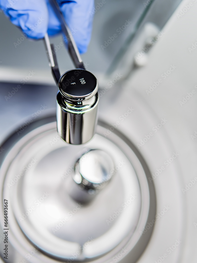 A operator's hand is holding steel calibration weight to place on the analytical balance. Concept of quality control in a laboratory. A operator's hand is holding steel calibration weight to place on the analytical balance. Concept of quality control in a laboratory.