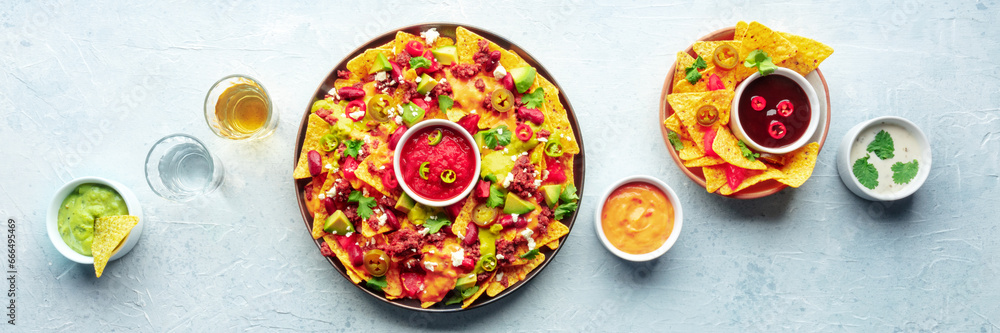 Loaded nachos panorama. Mexican nacho chips with beef, overhead flat lay shot with guacamole sauce, cheese salsa, tequila drinks, on a slate background