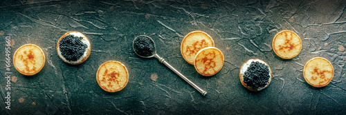 Blinis with black caviar and cream cheese panorama on a black slate background, mini pancakes, festive menu banner, overhead flat lay shot