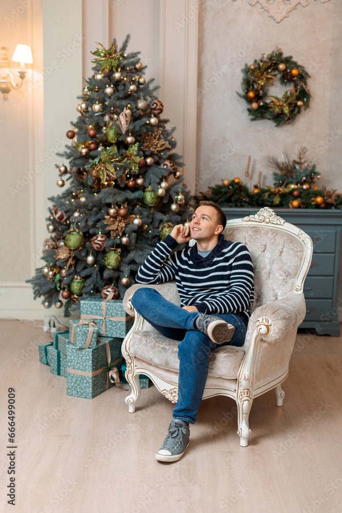 A happy men is sitting in a chair near the Christmas tree at home A happy men is sitting in a chair near the Christmas tree at home