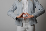 frau im engen business outfit weiße jeans blaue jacke zeigt mit den händen ein herz herzform herzen symbolsich liebe verliebt danke geste handherz herzhand