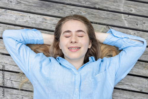 Top view of happy student young female with braces lying on a wooden background. photo