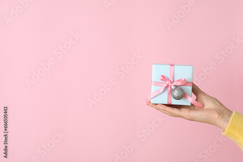 Gift box in female hand on pink background, space for text photo