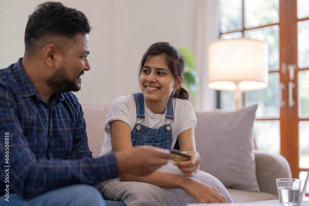 Indian couple shopping online with laptop and credit card from home, sitting on sofa in living room Indian couple shopping online with laptop and credit card from home, sitting on sofa in living room