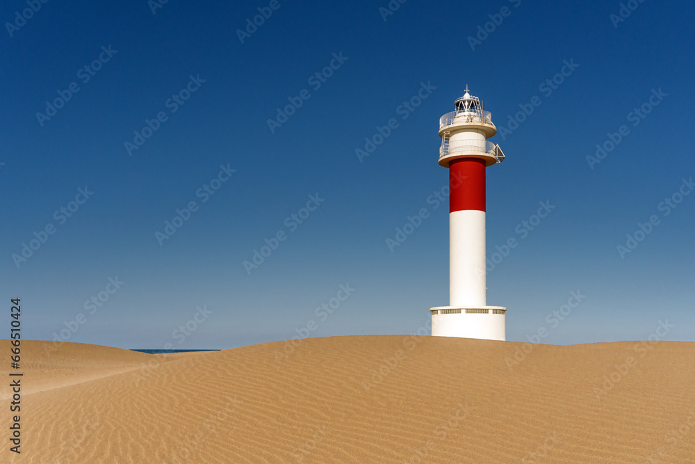 Lighthouse of Delta del Ebro among the Fangar beach dunes at sunset in a sunny day