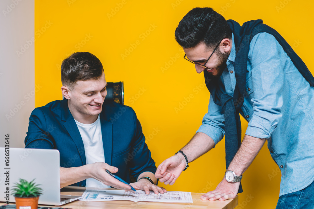 Happy cheerful male architects analyzing sketch for new design project during work time in office Happy cheerful male architects analyzing sketch for new design project during work time in office