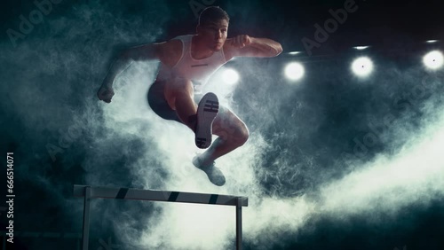 Aesthetic Dark Studio Sports Footage with Super Slow Motion Speed Ramp and Smoke Effects. Talented Male Hurdler Jumping Over Obstacle, Racing Against Time and Setting a New Sprint Record photo