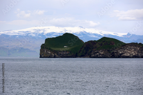 The Icelandic island of Ellidaey in the Vestmannaeyjar archipelago with the Eyjafjallajokull glacier in the background photo