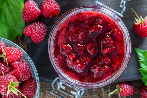 Red raspberry jam and fresh raspberry on a wooden table. Rustic style, closeup, top view