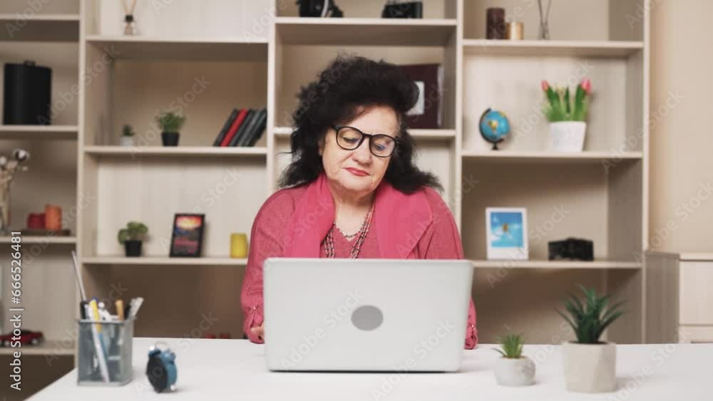 old woman, with a sad expression, finishes her work on the laptop and, taking off her glasses, massages her neck old woman, with a sad expression, finishes her work on the laptop and, taking off her glasses, massages her neck