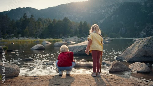 Kids play with water on mountain lake shore at vacation travel on sunset