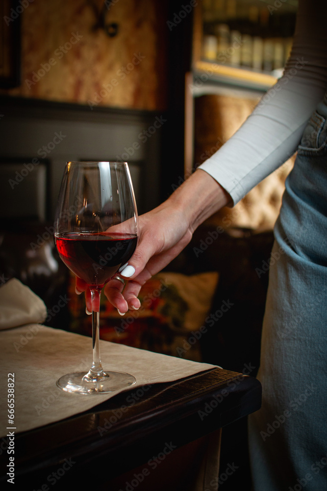 Hand holding a glass of red wine in a cozy bar setting Hand holding a glass of red wine in a cozy bar setting