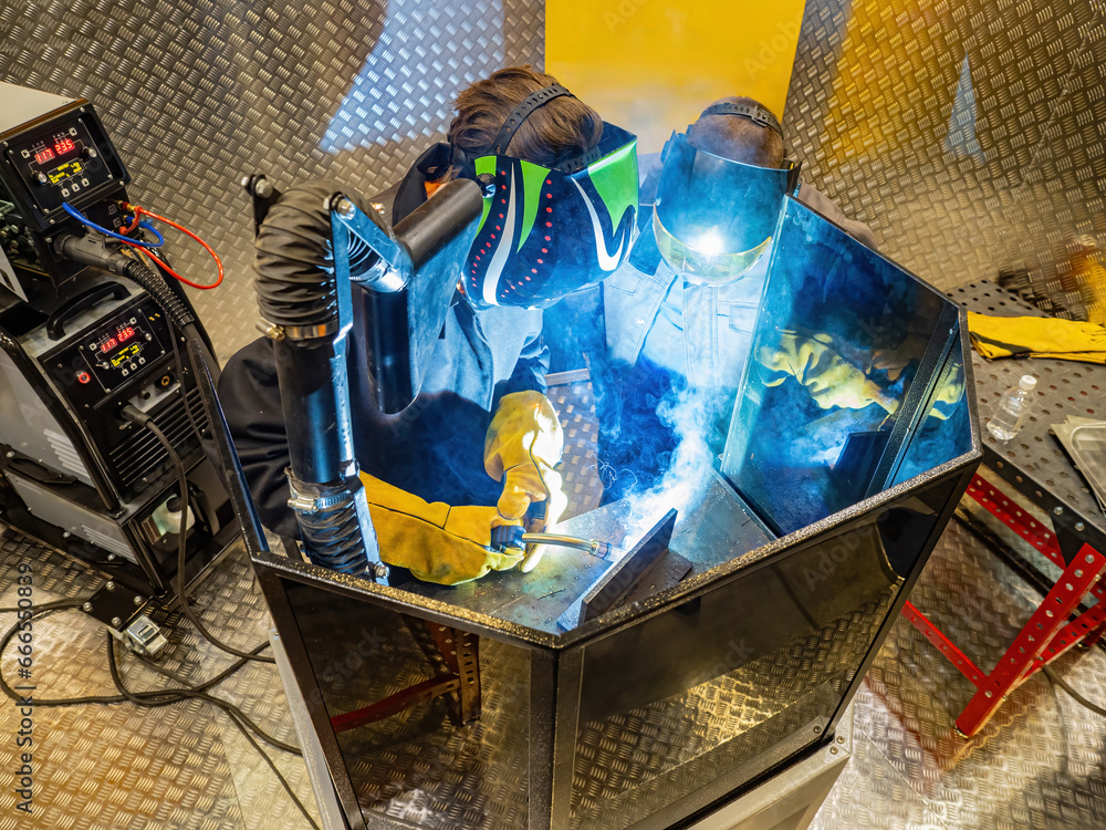 Foto de Two welders are working indoors. Men in masks for soldering