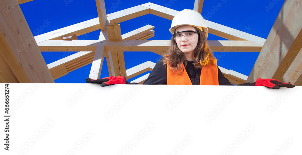 Woman builder with white banner. Architect girl near cope space. Builder under wooden frame house. Woman at construction site. Builder demonstrates place for inscription. Engineering career