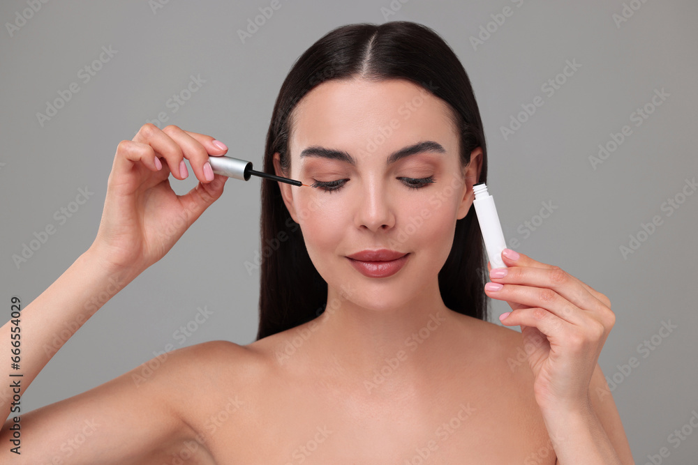 Fototapeta premium Beautiful woman applying serum onto her eyelashes on grey background. Cosmetic product