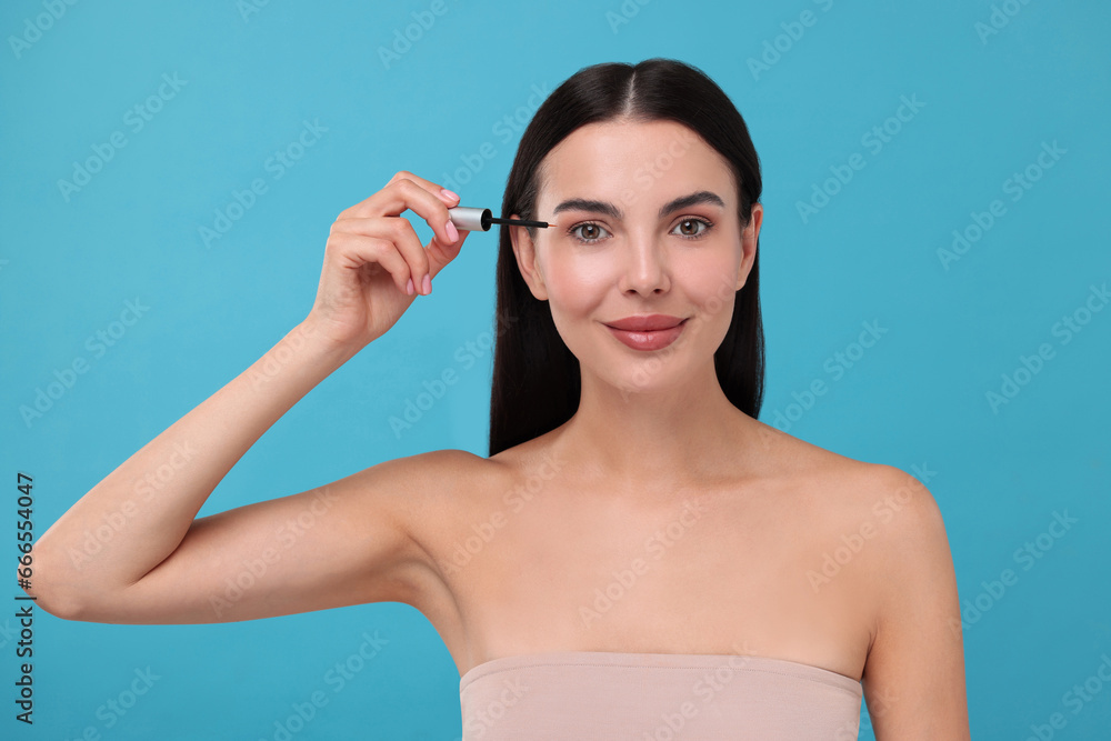 Beautiful woman applying serum onto her eyelashes on light blue background. Cosmetic product Beautiful woman applying serum onto her eyelashes on light blue background. Cosmetic product
