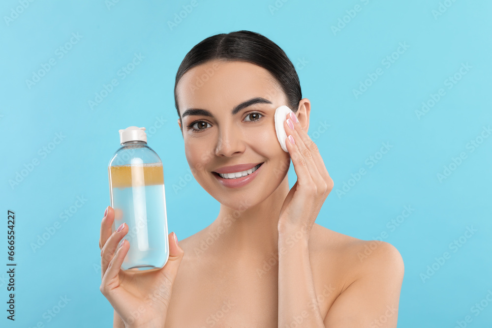 Beautiful woman removing makeup with cotton pad on light blue background Beautiful woman removing makeup with cotton pad on light blue background
