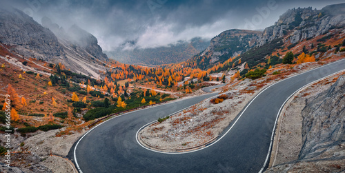 Misty autumn view of Tre Cime Di Lavaredo National Park with winding road. Gloomy evening scene of Dolomite Alps, Auronzo Di Cadore location, Italy, Europe. Beauty of nature concept background.