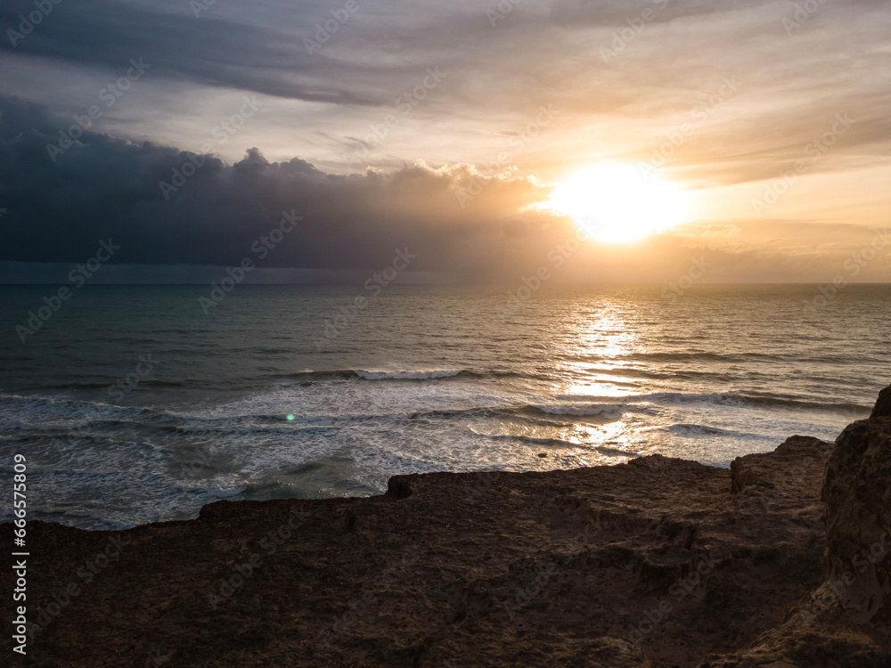 sunrise in the ocean with blue and orange sky with dramatic clouds seen from the cliff, at Pipa beach - Brazil