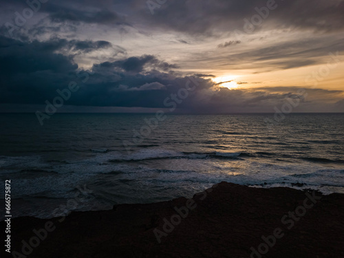 sunrise in the ocean with blue and orange sky with dramatic clouds seen from the cliff  at Pipa beach - Brazil