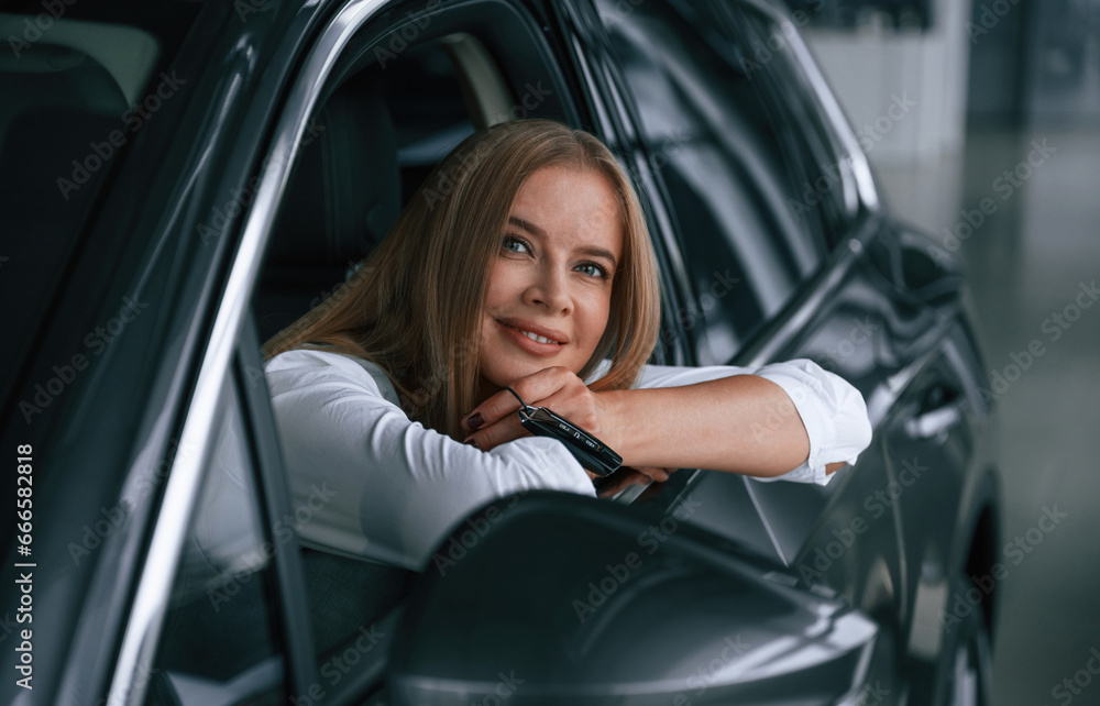 Looking from the opened window. Woman is sitting in a car and driving it Looking from the opened window. Woman is sitting in a car and driving it