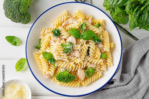 Delicious broccoli and chicken fusilli pasta with parmesan cheese and fresh basil in a bowl on a white wooden background. Healthy comfort food.