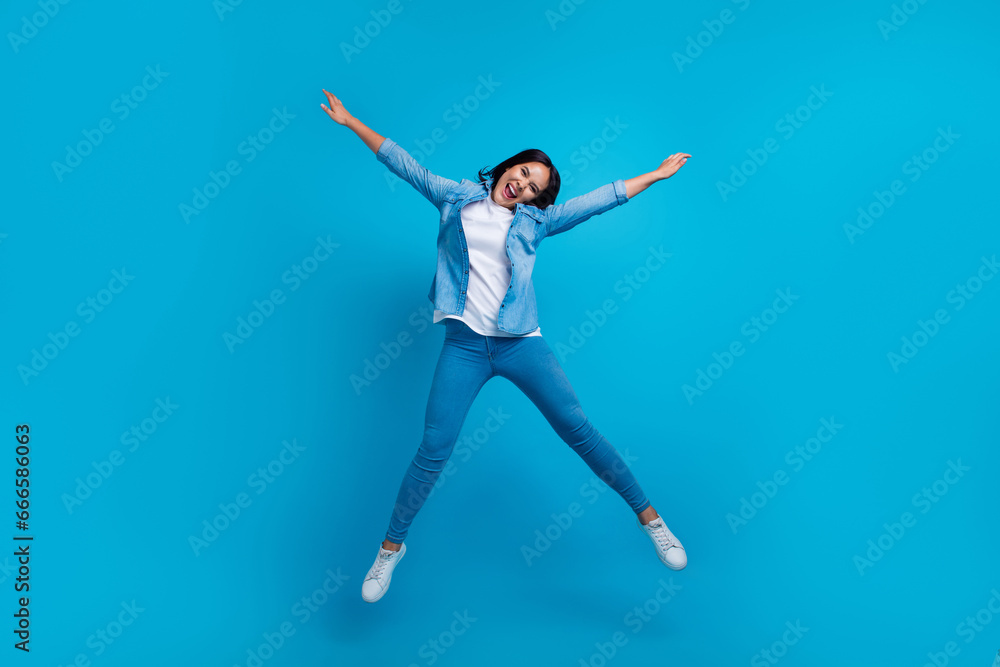 Full size photo of overjoyed crazy woman with straight hairdo dressed jeans shirt jumping high hands up isolated on blue background