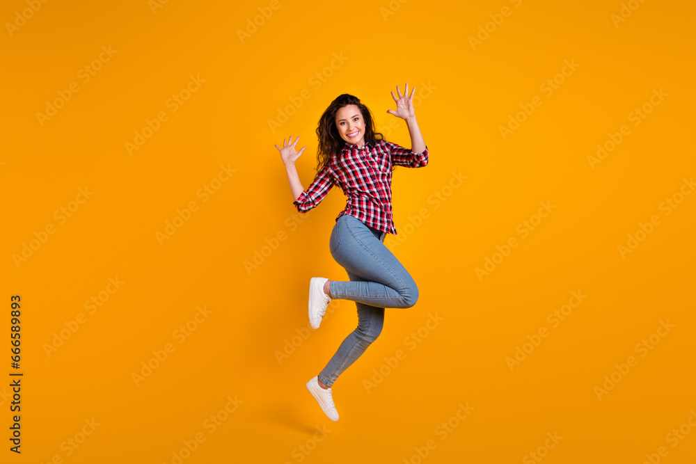 Full length photo of good mood cheerful person wear plaid shirt jeans trousers jumping raising palms up isolated on yellow background