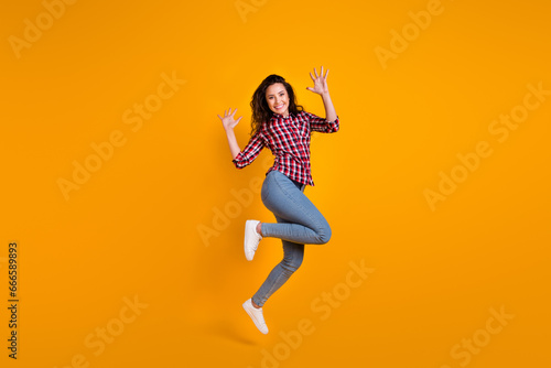 Full length photo of good mood cheerful person wear plaid shirt jeans trousers jumping raising palms up isolated on yellow background photo