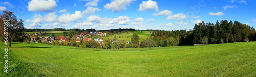 Panorama von weiter Landschaft im Schwarzwald im Herbst mit Wiese, Bäumen und Wohnhäusern bei blauem Himmel und weißen Wolken