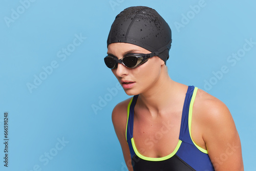 Girl in black swimming goggles on her face and black cap posing on blue background, professional sport concept, copy space