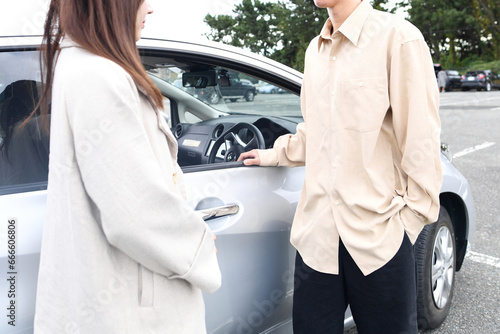 車の前で会話をする男女のアジア人カップル