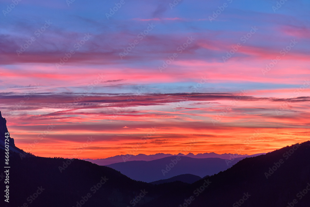 Red sunset over Passo delle Erbe with background of Dolomite peaks. Sky colored with shades of red, orange and blue, aerial view from high altitude.
