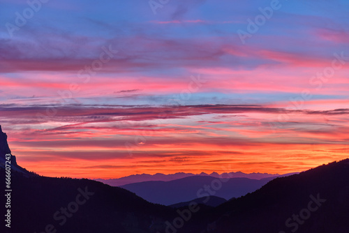 Red sunset over Passo delle Erbe with background of Dolomite peaks. Sky colored with shades of red, orange and blue, aerial view from high altitude. © Martin Mecnarowski