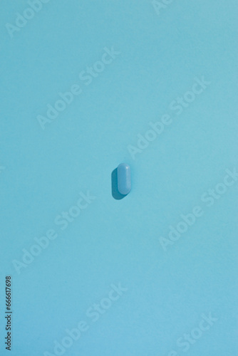 A flat-lay composition on a serene blue background with a light blue pill in the center of the photo. Sense of minimalism, healthcare, and simplicity. Medicament photoshoot. Monochromatic blue.