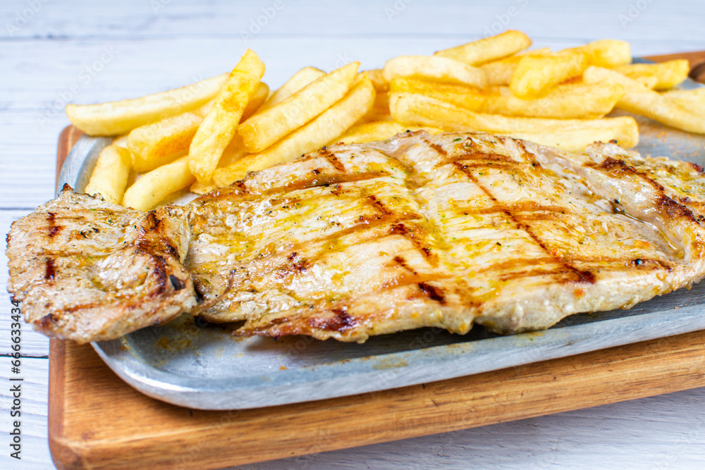 Tray of roast pork, accompanied by arepa with cheese, French fries and chimichurri