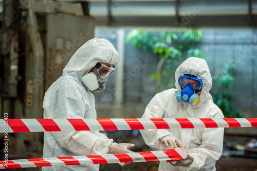 Man inspector scientist investigate chemical gas leak spill with safety face mask PPE suit in area closed barricade security red white tape. danger area infected toxic leak spill cross stripe ribbon photo