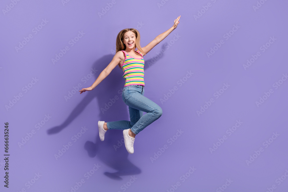 Full size photo of pretty teenager blonde girl jump hands fly wings plane wear trendy striped outfit isolated on purple color background
