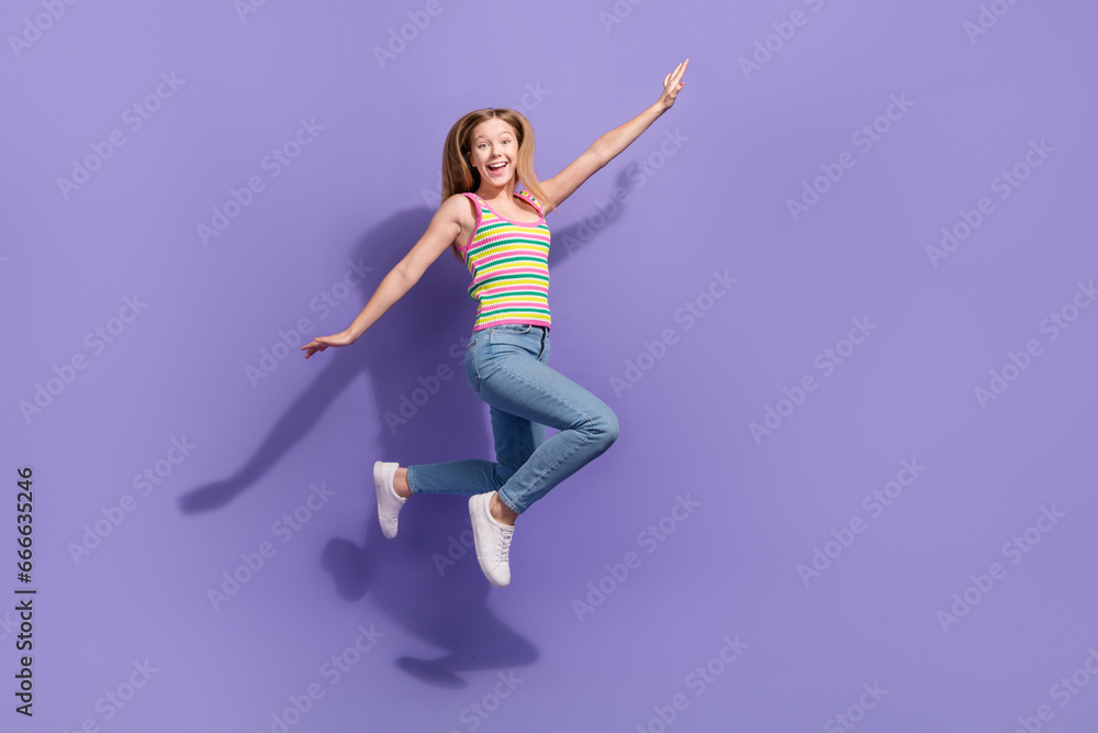 Full size photo of pretty teenager blonde girl jump hands fly wings plane wear trendy striped outfit isolated on purple color background Full size photo of pretty teenager blonde girl jump hands fly wings plane wear trendy striped outfit isolated on purple color background