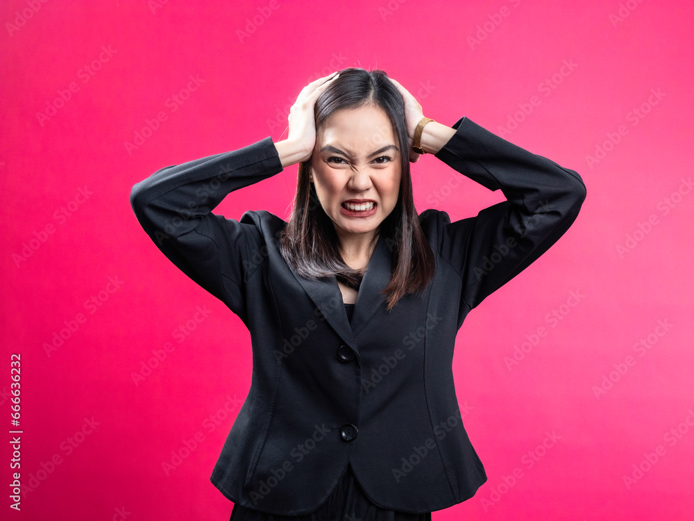 Portrait of an Asian Indonesian woman wearing a black work shirt, feeling emotional, having a headache, and holding her head. Isolated against a magenta background. Portrait of an Asian Indonesian woman wearing a black work shirt, feeling emotional, having a headache, and holding her head. Isolated against a magenta background.