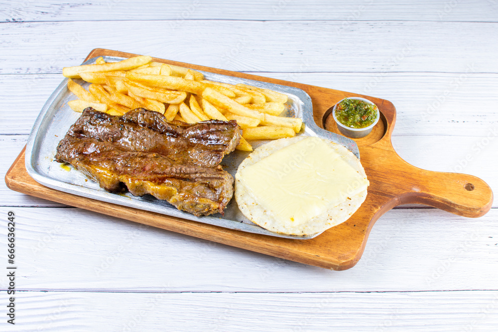 Tray of roasted haunch tip, accompanied by arepa with cheese, French fries and chimichurri